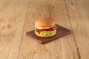 Brekkie burger with egg, bacon, cheese and avocado made with Tip Top Grill House Classic Burger Buns on a wooden board.