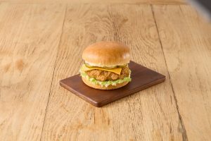 Crispy chicken burger with cheese, lettuce and pickles made with Tip Top Grill House Classic Burger Buns on a wooden board.